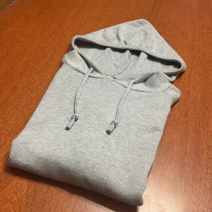 Ljusgrå merinoull hoodie - En stilren ljusgrå hoodie med huva och snören. Tröjan har långa ärmar, ribbade muddar och är tillverkad i mjukt merinoullsmaterial. Perfekt för chill dagar eller när du vill ha en enkel och clean look. passar perfekt med ett par mörkblå jeans 👖.