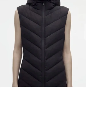 Svart zara väst - Säljer en svart dunväst med huva och dragkedja framtill. Har haft på mig den en sesången så den är i bra skick. Västen har ett quiltat mönster i V-form och är ärmlös med en stilren look. Perfekt för lager-på-lager och passar dig som gillar sportig och enkel stil.