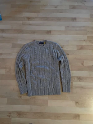 Grå kabelstickad Ralph lauren tröja  - En riktigt snygg grå kabelstickad Ralph lauren tröja. Använd fåtal gånger men fortfarande i riktig bra skick utan något tecken på användning!! Hör av dig vid frågor!