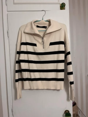 Randig half zip tröja från Vero Moda - Snygg stickad tröja från Vero Moda i beige med svarta ränder. Tröjan har en bred krage och en half zip med rund metallring. Långärmad och ribbad vid krage, ärmslut och nederkant. Perfekt för chill höst- och våroutfits. Något popprig men annars fin! Pris går att diskutera!💕