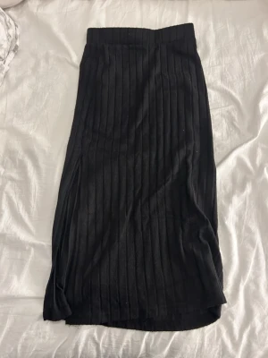 Svart långkjol från SHEIN XS - Säljer en svart långkjol från SHEIN i storlek XS. Kjolen har ett snyggt ribbat mönster och är gjord i mjuk polyester med lite stretch. Den har en slits på sidan som ger en cool vibe och passar perfekt till sneakers eller boots.