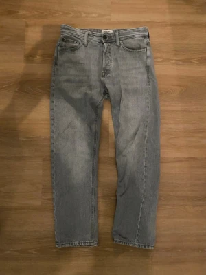 Grå relaxed jeans från Jack & Jones - Säljer ett par grå jeans från Jack & Jones, modell Relaxed/Chris. De har en avslappnad passform med raka ben och klassisk femficksdesign. Jeansen är tillverkade i bomull och har en enkel look som funkar till många stilar.
