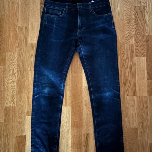 Mörkblå jeans från Uniqlo, 32/34 - Snygga mörkblå jeans från Uniqlo i klassisk femficksmodell. Jeansen har raka ben och normal passform, tillverkade i stretchig denim. Har inga defekter. Och det är riktig denim så blir  snyggare om används mer 