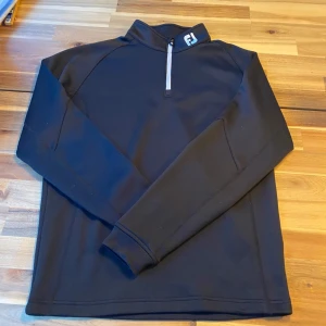Halfzip FootJoy - Säljer en svart tröja från FootJoy i storlek S. Tröjan har en dragkedja vid halsen och är tillverkad i 100% polyester. Perfekt för en sportig look med långärmade ärmar och en stilren design. Nypris ca 1000kr använd fåtal gånger inga defekter