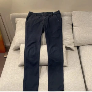 Mörkblå chinos från Dondup - Snygga mörkblå chinos från Dondup med klassisk rak passform. Byxorna har bälteshällor, sidofickor och bakfickor med knapp. Tillverkade i mjuk bomull för en skön känsla och stilren look. Perfekta för dig som gillar en clean och enkel stil.