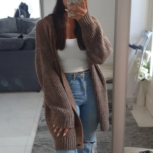 Brun ribbstickad kofta i oversized modell - Mysig brun ribbstickad kofta i oversized passform. Koftan har långa ärmar och knappar framtill, perfekt att slänga över en topp för en chill look. Tjockt och mjukt material som håller dig varm under kyliga dagar.