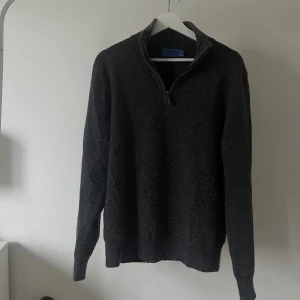  stickad halfziptröja från C&Jo - Mörkgrå stickad tröja från C&Jo med half zip och hög krage. Tröjan har lång ärm och en klassisk, enkel design som passar perfekt till jeans. Mjuk och skön känsla, perfekt för kyligare dagar. Tröjan är lite nopprig men går att lösa enkelt om man har en noppbortagare! Modellen 180cm.