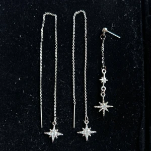 Silvriga örhängen med stjärnhänge - Långa, tunna kedjeörhängen i silverfärg med hängande stjärna dekorerad med små glittrande stenar. Snygg och modern design som ger en cool touch till din look. Perfekta för dig som gillar unika detaljer och vill sticka ut. Köpta i Spanien