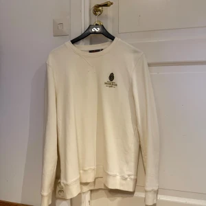 Vit sweatshirt från Morris - Säljer en stilren vit sweatshirt från Morris med broderad logga på bröstet. Tröjan har rund halsringning, långa ärmar och ribbade muddar. Perfekt för dig som gillar klassisk och clean stil.