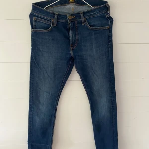 Lee Luke jeans W30 L32 blå - Säljer ett par Lee Luke jeans i klassisk blå tvätt med snygga slitningar. Modellen har smal passform, fem fickor och gylf med dragkedja. Tydliga Lee-detaljer på bakfickan och patch i midjan. Perfekta jeans för dig som gillar en modern look.