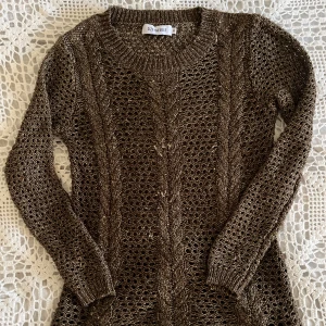 Brun stickad tröja från Size 8 Needle - Snygg brun stickad tröja från Size Needle med flätstickat mönster och hålstickad design. Tröjan har rund halsringning och långa ärmar, perfekt för lager-på-lager. Guldtråd inflätad i garnet vilket ger en unik look! 