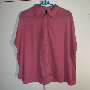 Rosa skjorta från H&M, storlek S - Rosa skjorta från H&M i storlek S. Skjortan har klassisk krage, knappar hela vägen framtill och är tillverkad i ett lätt och luftigt material. Passformen är loose och skjortan har korta ärmar utan manschett. Perfekt för dig som gillar färg och enkel stil.