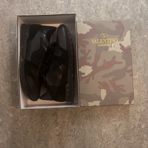 Valentino Garavani Rockrunner sneakers - Snygga svarta Valentino Garavani Rockrunner sneakers med tonat kamouflagemönster. Skorna har klassisk snörning, rund tå och platt sula. Materialmix av skinn och syntet ger en exklusiv känsla. Perfekta för dig som vill ha en stilren och lyxig sneaker.