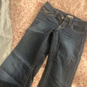 Mörkblå jeans med slitna kanter - Snygga mörkblå jeans med kontrasterande vita sömmar och slitna, fransiga kanter vid bensluten. Modellen har klassiska fem fickor, varav bakfickorna har lock och knapp. Jeansen har låg midja och är tillverkade i jeansmaterial.