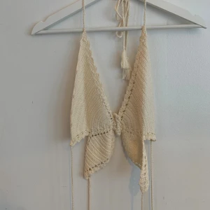 Beige virkad linnetopp från Urban Outfitters - Superfin beige virkad linnetopp med knytband i nacken och rygg. Från Urban Outfitters limited edition kollektion. Toppen har en v-ringad form och dekorativa kanter med kreativa spetsdetaljer. Perfekt för varma dagar och ger en boho-vibe till din outfit. Aldrig använd. 