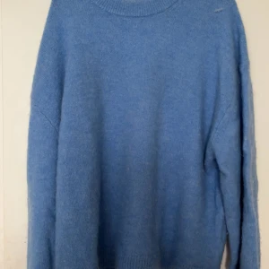 Blå stickad tröja med rund hals - Mysig blå stickad tröja med rund hals och långa ärmar. Perfekt för kyliga dagar och enkel att matcha med jeans eller kjol. Tröjan har en klassisk passform och ribbade muddar vid hals, ärmslut och nederkant.