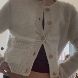 Beige stickad kofta - Mysig beige stickad kofta med guld knappar, och två fickor framtill. Koftan har ribbade detaljer vid kanter och fickor.❤️ny skick skulle säga att den passar dom som har xs-s