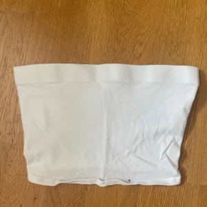Vit bandeau tubtopp från H&M Divided XS - Enkel och stilren vit bandeau tubtopp från H&M Divided i storlek XS. Toppen är ärmlös och axelbandslös, tillverkad i mjuk bomull med stretch för en bekväm passform. Perfekt att matcha med jeans eller kjol för en clean look.