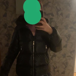 Svart Moncler pufferjacka med huva - Säljer en svart pufferjacka från Moncler med glansig finish och stor huva. Jackan har två snedställda fickor med dragkedja och coolt Moncler-tryck på insidan. Perfekt för kalla dagar och riktigt snygg streetstil. En limited edition collab med Sven Giubotto🥰 nypris 11 000kr