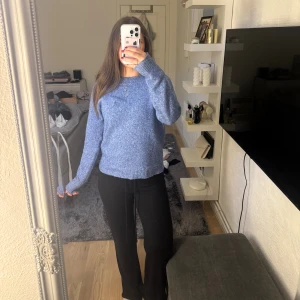 Blå stickad tröja med rund hals - Mysig blå stickad tröja med rund halsringning och långa ärmar. Tröjan har en lätt melerad look och ribbade muddar vid ärmslut och nederkant. Perfekt för lager-på-lager under kyliga dagar.