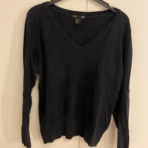 Svart v-ringad tröja  - Svart v-ringad stickad tröja från H&M med långa ärmar och snygga knappar vid ärmsluten. Perfekt basic-plagg med normal passform som funkar till allt. Mjuk och skön känsla tack vare bomullsmaterialet. Storlek S.