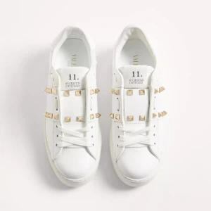 Valentino Rockstud vita sneakers - Snygga vita Valentino Rockstud sneakers i skinn med ikoniska guldiga nitar på ovandelen. Klassisk rund tå, platt sula och snörning framtill. Perfekt för dig som vill ha en clean men edgy look med exklusiv känsla. Nästan som nya! Har kvar kartong mm. Nypris 8515💕
