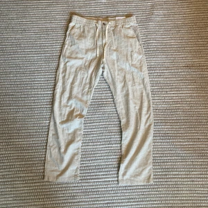 Helt nya linnebyxor från H&M Regular Fit - Nypris 400 kr. Ett par byxor i luftig, vävd bomulls- och linblandning. Byxorna har klädd resår och dragsko i midjan, sidfickor och stolpficka bak. Gylf med dragkedja och knapp. Regular Fit för en bekväm, klassisk silhuett. I bomulls- och linblandningar kombineras bomullens mjukhet med linnets slitstyrka, vilket ger ett följsamt tyg med textur och god andningsförmåga. FÄRG:Crèmevit. Storlek M Art.nr: 1253401001