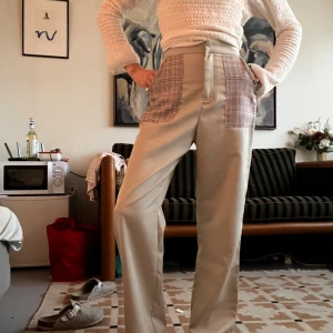 Gröna byxor med rutiga fickor - Unika gröna byxor med raka ben och stora rutiga fickor framtill i rött, svart och vitt. Hög midja och relaxed fit. Snygg kontrast mellan det släta tyget och de rutiga detaljerna. Perfekta för dig som vill sticka ut med en cool och personlig stil.