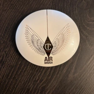 Charlotte Tilbury Airbrush Brightening Powder - Charlotte Tilbury Airbrush Brightening Flawless Finish i färgen Tan-Deep. Kompakt puder i en rund, vit dosa med spegel och snyggt vingmönster på locket. Ger en ljus och jämn finish till ansiktet. Perfekt för att sätta sminket och ge glow. Färg: Tan-deep