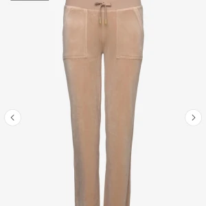 Beige mjukisbyxor med snörning från Juicy Couture - Snygga beige mjukisbyxor med raka ben och breda fickor framtill. Byxorna har en bekväm midja med snörning och är gjorda i mjukt material som ger en chill vibe. Perfekta för en avslappnad stil.
