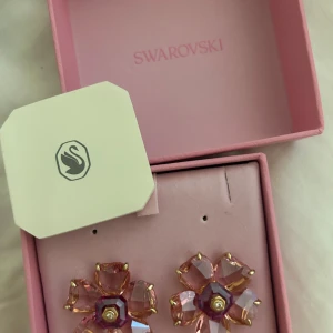 Swarovski blommiga örhängen rosa - Superfina örhängen från Swarovski i form av blommor med rosa kristaller och guldfärgade detaljer. De har en glittrig finish och kommer i original ask. Perfekta för dig som vill sticka ut med ett unikt smycke.