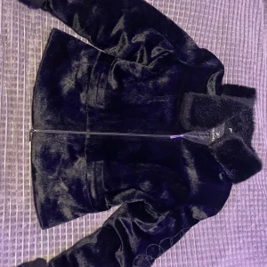 Svart pälsjacka från Prunel - Säljer en svart pälsjacka från Prunel med dragkedja framtill och stor fluffig krage. Jackan har ett broderat motiv på ena ärmen med mjuk och glansig yta💗