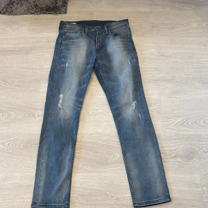 Levi's 511 blå jeans W31 L32 - Säljer ett par Levi's 511 jeans i klassisk blå tvätt med slitningar och lätt distressed look. Modellen är slim och har fem fickor, normal midja och raka ben. Jeansen är tillverkade i bomull och har den ikoniska Levi's-lappen bak.