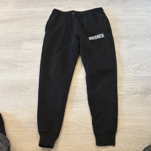 Svarta mjukisbyxor från Hoodrich XS - Svarta mjukisbyxor från Hoodrich i storlek XS. Byxorna har resår och snörning i midjan, muddar vid bensluten och vit HOODRICH-logga på ena benet. Perfekta för chill eller streetwear. Mjukt material och två fickor framtill.