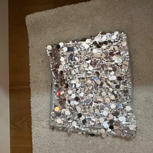 Silver glittrig minikjol från Cider - Supersnygg kortkjol från Cider i silver med massor av stora paljetter som ger en maxad glittrig effekt. Kjolen är figurnära och har en slät, mjuk insida för extra komfort. Perfekt för dig som vill sticka ut och glänsa.