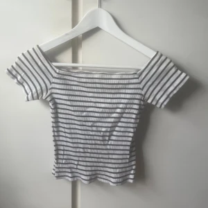 Randig ribbad offshoulder topp - Säljer en vit och marinblå randig topp med ribbad struktur. Modellen är offshoulder med korta ärmar och croppad passform. Inte helt säker på storlek men skulle säga xs🥰