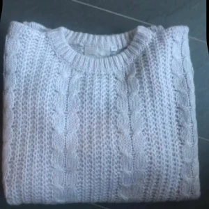 Ljusgrå stickad tröja Nuova Moda ny  - Mysig ljusgrå stickad tröja från Nuova Moda med klassiskt flätmönster. Tröjan har rund halsringning och långa ärmar, perfekt för kyliga dagar. Oversized passform för en avslappnad vibe. Oanvänd 