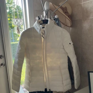 Vit pufferjacka från Ralph Lauren - Säljer en snygg vit pufferjacka från Ralph Lauren med diskret logga på ärmen. Jackan har dragkedja framtill och en liten ficka med knappar på ena ärmen. Perfekt för kyliga dagar och riktigt stilren look.Någon minifläck som man ej tänker på. Hör av er för fler bilder🥰