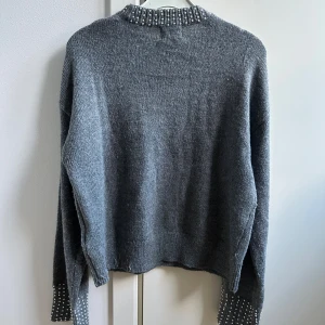 Grå stickad tröja med pärlor från H&M - Snygg grå stickad tröja från H&M i London med pärldetaljer runt halsringningen och vid ärmsluten. Tröjan har långärmad passform och är mjuk och skön att bära. Perfekt för dig som gillar lite extra detaljer på din outfit. Storlek S. Använd en gång! Super bra för höst och vinter!💗💗💗💗 