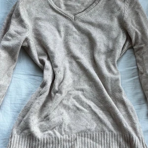 Beige stickad v-ringad tröja - Mysig beige stickad tröja med v-ringning och långa ärmar. Tröjan har bred ribbad kant nedtill som ger en snygg detalj. Perfekt för dig som gillar enkel och stilren design med en soft vibe.