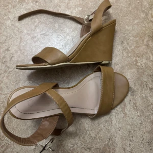 Bruna kilklackade sandaler - Enligt mig skit snygga bruna sandaler med kilklack. Storlek 36, använd ett par gånger men så gott som nya, köpta utomlands. 