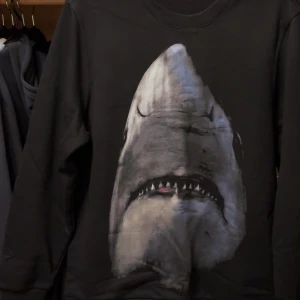 Svart sweatshirt givenchy  - Cool svart sweatshirt med en stor, realistisk haj på framsidan. Tröjan har rund hals och långa ärmar, perfekt för dig som vill sticka ut med ett unikt tryck. Passar till både jeans och sneakers för en avslappnad look.