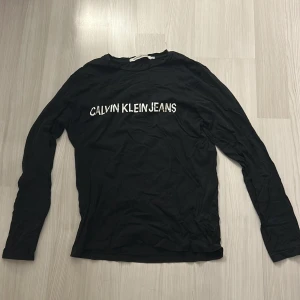 Svart långärmad tröja Calvin Klein Jeans - Svart långärmad tröja från Calvin Klein Jeans med vit logga tryckt över bröstet. Klassisk rund halsringning och mjukt bomullsmaterial som är skönt mot huden. Perfekt för en clean och stilren look.