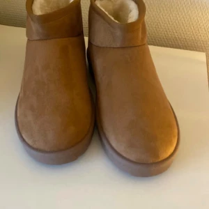Bruna boots med foder från Noixx - Mysiga bruna boots från Noixx i storlek 37. Skorna har en mjuk och fluffig insida i syntetpäls och utsida i mockaimitation. Perfekta för kalla dagar med sin platta sula och rund tå. Enkla att dra på.