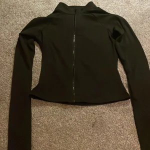 Svart slim sipp tröja  med dragkedja - Snygg svart sipp tröja med slim passform och hel dragkedja framtill. Jackan har hög krage och långa ärmar, perfekt för en clean och sportig look. Materialet känns lätt och smidigt, vilket gör den enkel att bära och matcha med olika outfits.