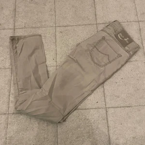 Gråa Jacob Cohën Jeans - Snygga beige byxor från Jacob Cohën i klassisk rak modell. Byxorna har fem fickor och diskreta sömmar, perfekta för en clean och stilren look. Tillverkade i mjukt bomullstyg som känns skönt mot huden.