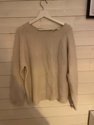 Beige stickad tröja från Vero Moda - Mysig beige stickad tröja från Vero Moda med bred ribbad kant i halsen och vid ärmsluten. Tröjan har en enkel, clean look och är långärmad med avslappnad passform. Perfekt att slänga på sig när det är kyligt ute.