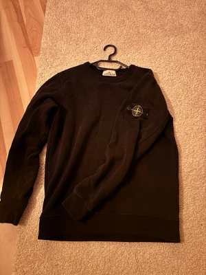 Svart sweatshirt från Stone Island - Säljer en svart sweatshirt från Stone Island med den klassiska loggan på vänster ärm. Tröjan har rund halsringning och långa ärmar. Tillverkad i mjuk bomull för skön vardagsstil. Perfekt till höst och vinter. Den har en liten liten reva i tyget som man ser på 4 bilden men enligt mig syns den knappt och märks knappt av. Pris går att diskutera vid snabb affär
