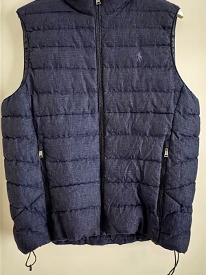 Mörkblå väst från Polo Ralph Lauren - Säljer en mörkblå dunväst från Polo Ralph Lauren i storlek M. Västen har quiltad design, dragkedja framtill och två sidofickor med dragkedja. Klassisk logga broderad på bröstet och justerbar nederkant med snörning. Perfekt för lager-på-lager under kyliga dagar.