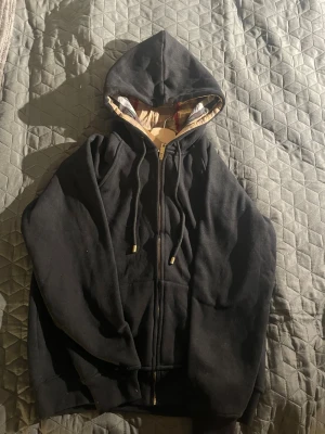 Svart hoodie med dragkedja  - Säljer denna Svarta hoodie med rutigt tryck då den tyvärr inte passade mig. Jag köpte Hoodien på plick tidigare och den är oanvänd med tagg kvar. Pass formen skulle jag säga är XS. Pris ej hugget i sten det är bara att fråga på! MVH Fille